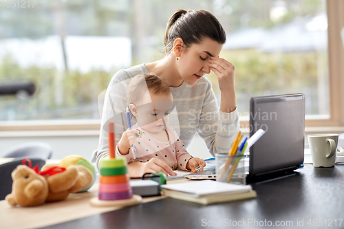 Image of tired mother with baby working at home office