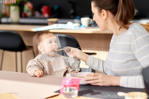 Image of happy mother feeding baby with puree at home