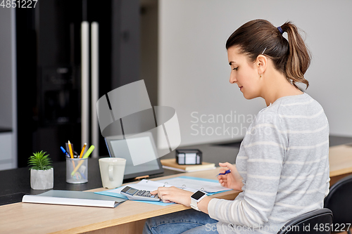 Image of woman with calculator and papers working at home