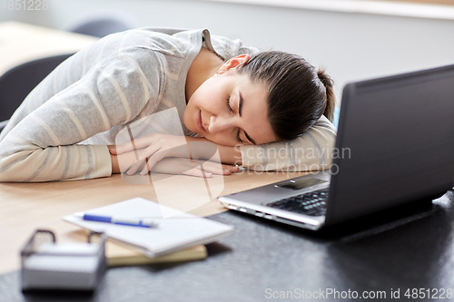 Image of tired woman sleeping on table with laptop at home