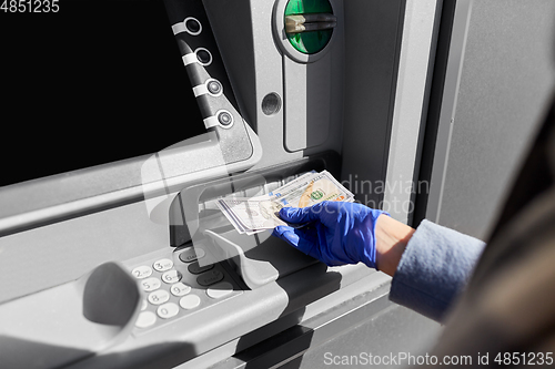 Image of hand in medical glove with money at atm machine