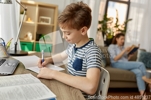 Image of student boy with book writing to notebook at home