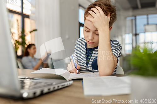 Image of student boy with book writing to notebook at home