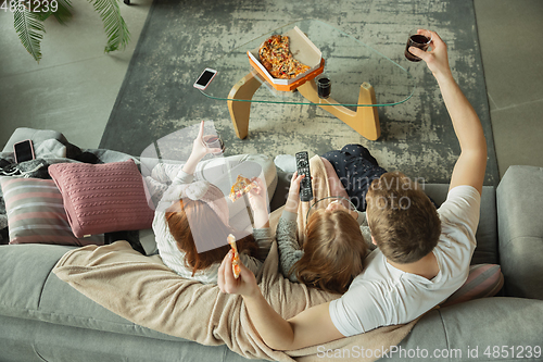 Image of Family spending nice time together at home, looks happy and cheerful, eating pizza. Top view.