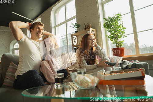 Image of Family spending nice time together at home, looks happy and excited, eating pizza, watching sport match