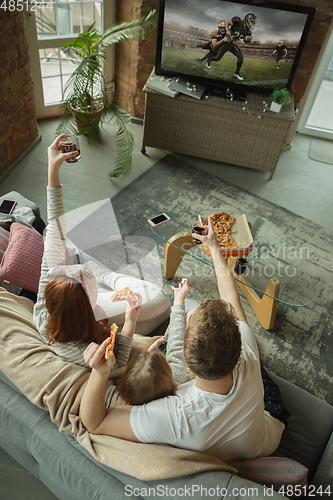 Image of Family spending nice time together at home, looks happy and excited, eating pizza, watching football match