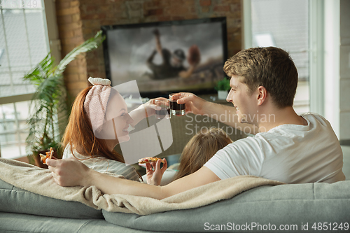 Image of Family spending nice time together at home, looks happy and excited, eating pizza, watching football match