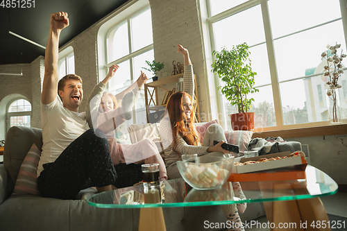 Image of Family spending nice time together at home, looks happy and excited, eating pizza, watching sport match