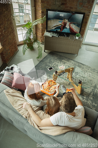 Image of Family spending nice time together at home, looks happy and excited, eating pizza, watching basketball match