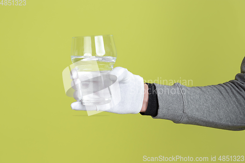 Image of Male hand wearing white glove holding glass of water isolated on yellow studio background