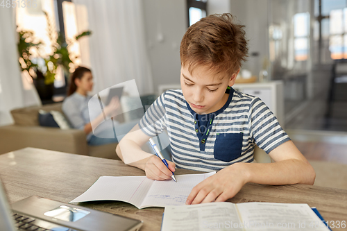 Image of student boy with book writing to notebook at home