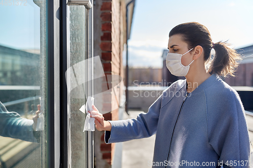 Image of woman in mask cleaning door handle with wet wipe