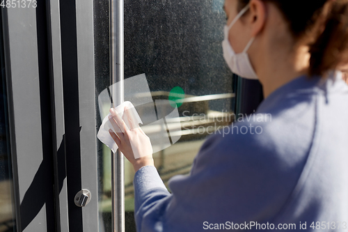 Image of woman in mask cleaning door handle with wet wipe