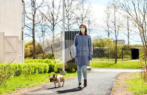 Image of woman in mask and gloves with dog walking in city