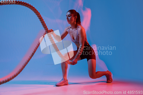 Image of Caucasian professional female athlete training on blue studio background in neon, mixed light. Muscular, sportive woman.