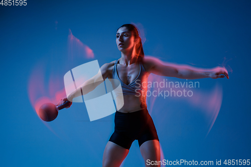 Image of Caucasian professional female athlete training on blue studio background in neon, mixed light. Muscular, sportive woman.