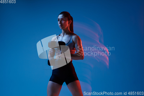 Image of Caucasian professional female athlete training on blue studio background in neon, mixed light. Muscular, sportive woman.