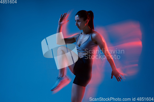Image of Caucasian professional female athlete training on blue studio background in neon, mixed light. Muscular, sportive woman.