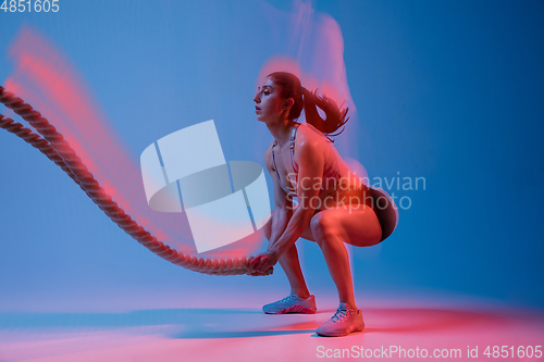 Image of Caucasian professional female athlete training on blue studio background in neon, mixed light. Muscular, sportive woman.