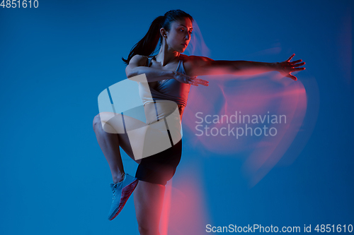 Image of Caucasian professional female athlete training on blue studio background in neon, mixed light. Muscular, sportive woman.