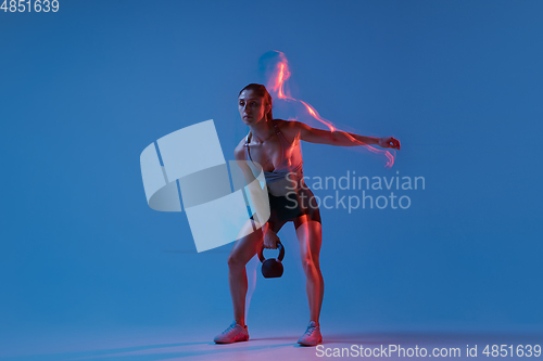 Image of Caucasian professional female athlete training on blue studio background in neon, mixed light. Muscular, sportive woman.