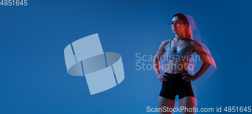 Image of Caucasian professional female athlete training on blue studio background in neon, mixed light. Muscular, sportive woman.