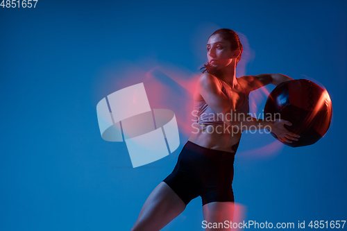 Image of Caucasian professional female athlete training on blue studio background in neon, mixed light. Muscular, sportive woman.