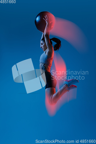 Image of Caucasian professional female athlete training on blue studio background in neon, mixed light. Muscular, sportive woman.