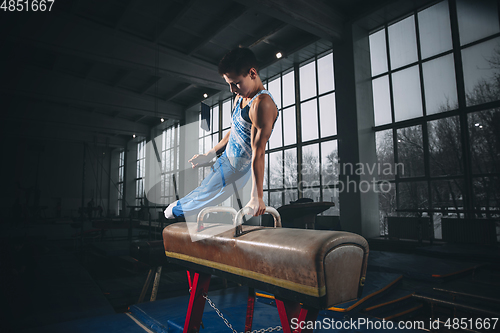 Image of Little male gymnast training in gym, flexible and active. Caucasian fit little boy, athlete in sportswear practicing in exercises for strength, balance.