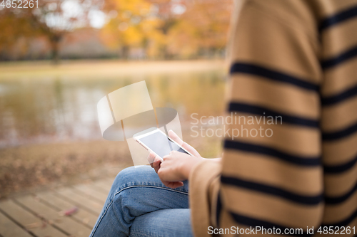 Image of Woman using cellphone at part in Autumn season