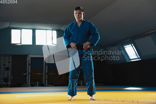 Image of Young judo fighter in kimono posing comfident in the gym, strong and healthy