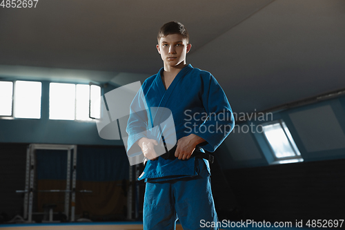 Image of Young judo fighter in kimono posing comfident in the gym, strong and healthy