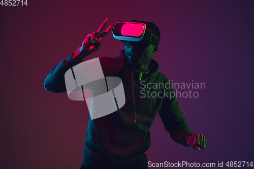 Image of African-american man\'s portrait in VR-headset isolated on gradient studio background in neon light