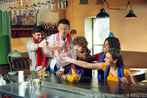 Image of Sport fans cheering at bar, pub and drinking beer while championship, competition is going