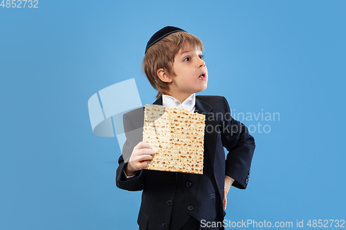 Image of Portrait of a young orthodox jewish boy isolated on blue studio background, meeting the Passover