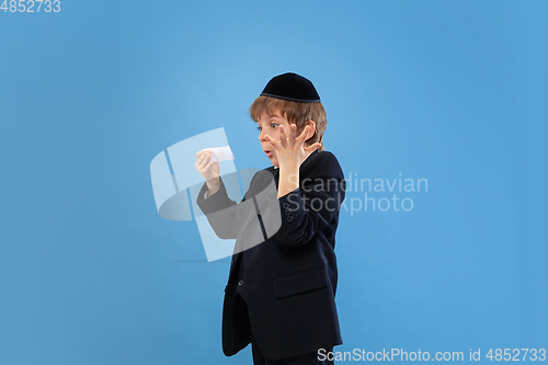 Image of Portrait of a young orthodox jewish boy isolated on blue studio background, meeting the Passover