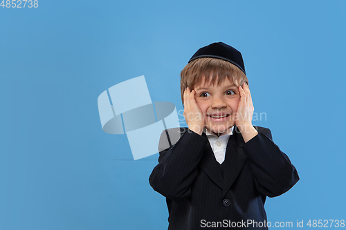 Image of Portrait of a young orthodox jewish boy isolated on blue studio background, meeting the Passover