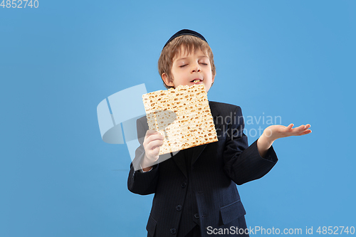 Image of Portrait of a young orthodox jewish boy isolated on blue studio background, meeting the Passover