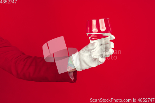 Image of Female hand in white glove holding glass of pure water on red background