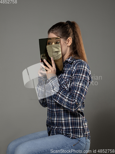 Image of Be safe and read to become someone else - woman covering face with book in face mask while reading on grey background