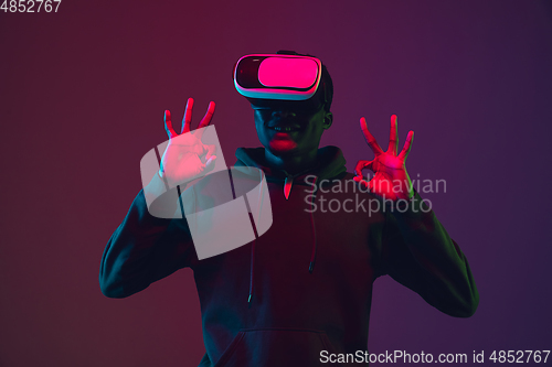 Image of African-american man\'s portrait in VR-headset isolated on gradient studio background in neon light