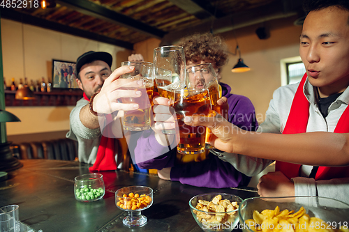 Image of Sport fans cheering at bar, pub and drinking beer while championship, competition is going