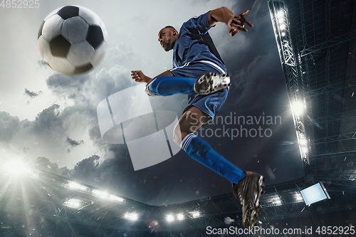 Image of Football or soccer player in action on stadium with flashlights, kicking ball for winning goal, wide angle