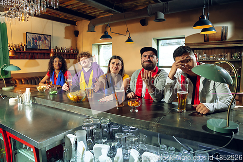 Image of Sport fans cheering at bar, pub and drinking beer while championship, competition is going