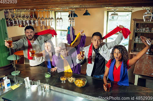 Image of Sport fans cheering at bar, pub and drinking beer while championship, competition is going