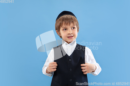 Image of Portrait of a young orthodox jewish boy isolated on blue studio background, meeting the Passover