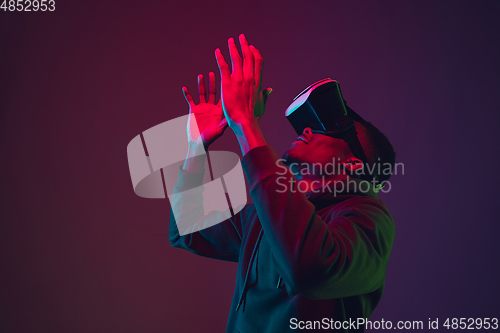 Image of African-american man\'s portrait in VR-headset isolated on gradient studio background in neon light