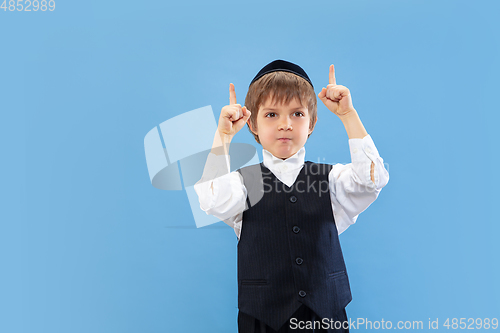 Image of Portrait of a young orthodox jewish boy isolated on blue studio background, meeting the Passover