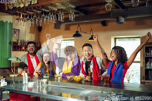 Image of Sport fans cheering at bar, pub and drinking beer while championship, competition is going