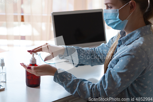 Image of Young woman in face mask disinfecting gadgets surfaces on her workplace